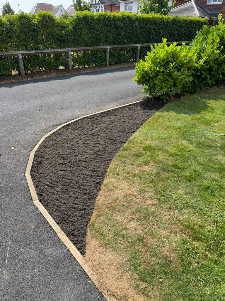 Newly edged border bed with fresh soil alongside a lawn and driveway